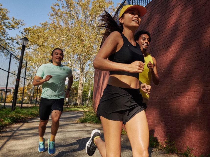 Three people running in a park wearing HOKA apparel.